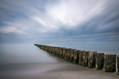 Wooden groyne in lake against cloudy sky