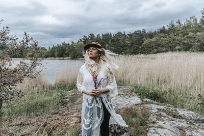 Young woman standing by plants against sky