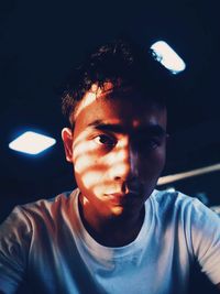 Close-up portrait of young man sitting in darkroom