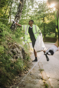 Teenage boy wearing reflective clothes picking plastic by plants