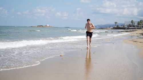 Young man jogging on a sandy beach on a sunny day in malia, crete island of greece.