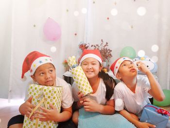 Portrait of siblings holding gifts while sitting at home during christmas