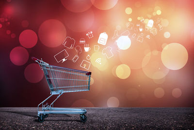 Digital composite image of icons emerging from shopping cart against illuminated background