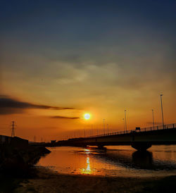 Silhouette bridge over calm river at sunset