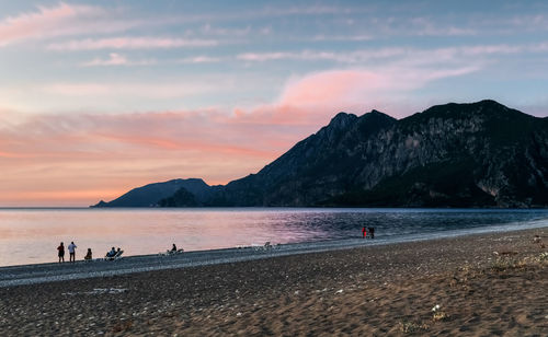 People on beach by mountains against sky during sunset
