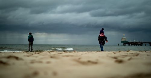 Surface level view of siblings at beach against cloudy sky