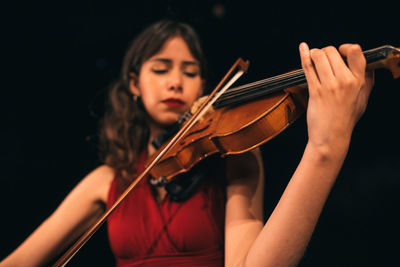 Woman in red dress playing violin with closed eyes during concert on stage in dark theater