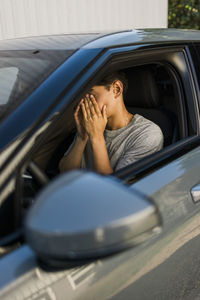 Tired young man covering face with hands sitting in car