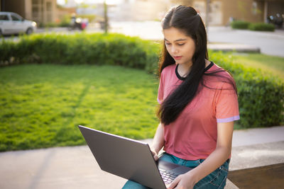 Portrait of young woman using laptop at park