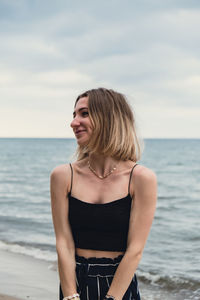 Young woman standing at beach against sky