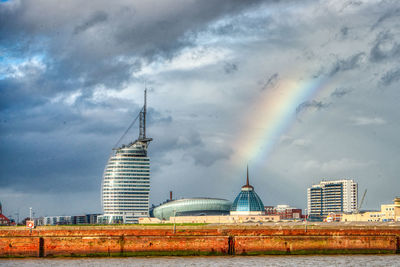 Rainbow over buildings in city against cloudy sky