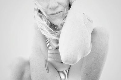 Midsection of mature woman wearing bikini while crouching against white background