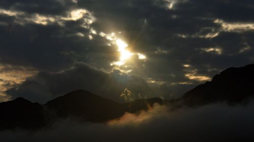 Scenic view of clouds over silhouette mountains against sky