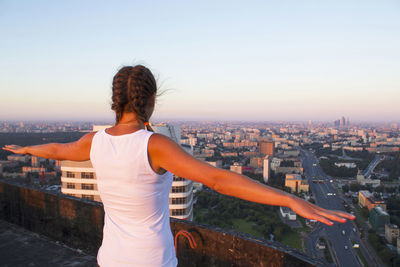 Rear view of woman standing by buildings against sky during sunset