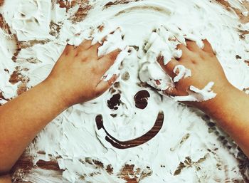 Cropped hand making face with cream on messy table