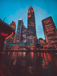 Illuminated modern buildings by river against sky