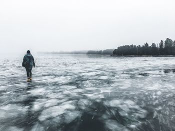 Rear view of woman walking on frozen lake against sky during winter