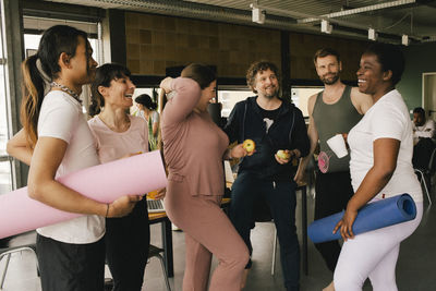 Happy multiracial colleagues standing with yoga mats and fruits in workplace