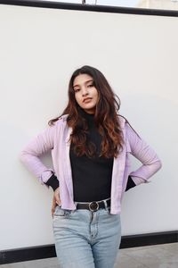 Portrait of young woman standing against wall