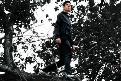 Low angle view of young man standing against tree