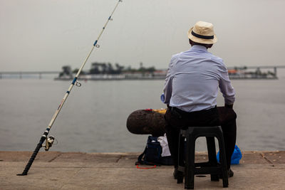 Rear view of man fishing in sea against sky