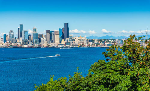 Sea by city buildings against blue sky