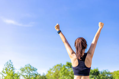 Rear view of woman with arms raised standing against sky