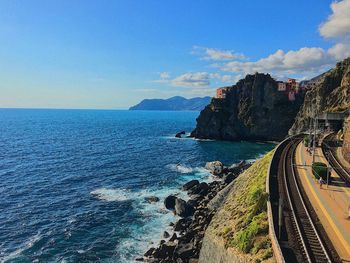 Railroad tracks on mountain by sea against sky