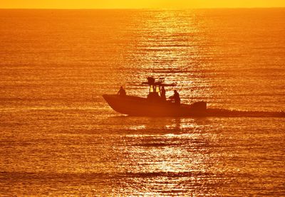 Silhouette boat sailing in sea against sky during sunset