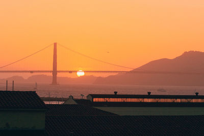Suspension bridge over sea against orange sky