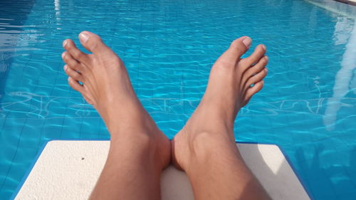 Low section of woman sitting on diving platform over swimming pool