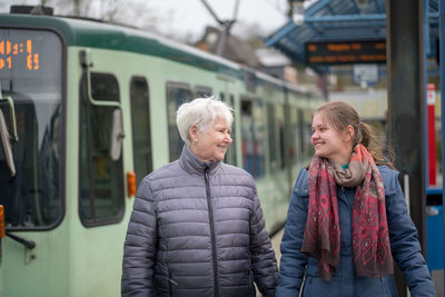 Smiling grandmother and granddaughter walking at railroad station platform