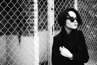 Young woman in sunglasses standing against chainlink fence