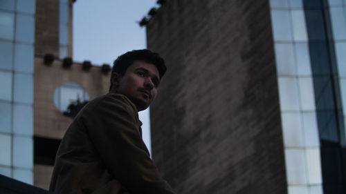 Low angle view of thoughtful young man standing against building in city