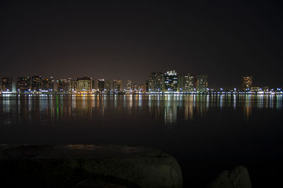 Illuminated buildings by river against sky at night