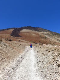 Rear view of man walking on mountain against clear blue sky