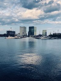 Sea by buildings in city against sky during sunset