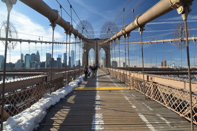 People walking on brooklyn bridge against blue sky during winter