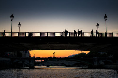 Silhouette bridge over river against sky during sunset