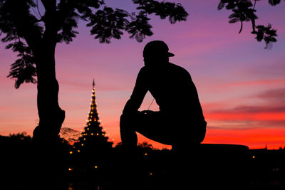 Silhouette man sitting against orange sky