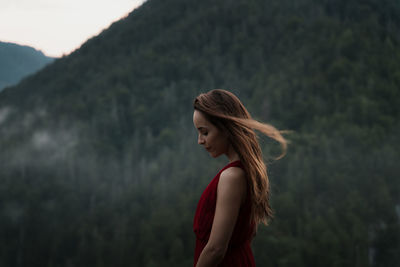 Side view of young woman standing against mountain