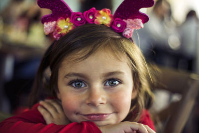 Close-up portrait of smiling girl wearing antlers while resting on table at cafe