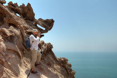 Man with camera on rock formation against sea and sky