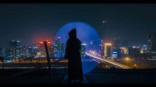 Rear view of man standing by illuminated buildings in city at night