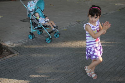 Portrait of smiling girl dancing near brother in baby stroller on footpath