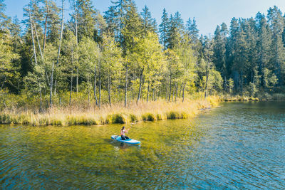 People floating on lake against trees in forest