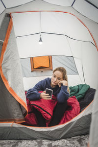 Teenage girl using smart phone while sitting in tent at camping site