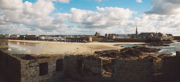 Scenic view of beach by buildings against cloudy sky