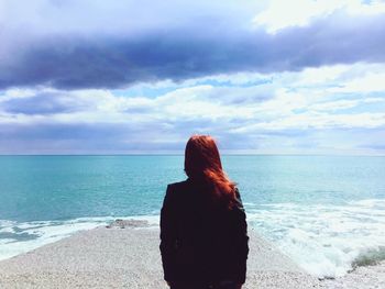 Rear view of woman standing at beach against cloudy sky on sunny day