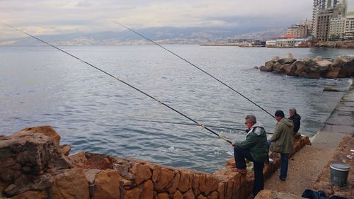 People fishing in sea against sky